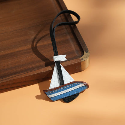 Blue and brown leather sailboat charm set on wooden tray