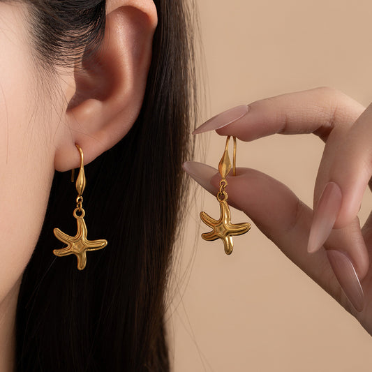  Close up of a model wearing gold starfish dangle earrings to demonstrate size and vacation style.