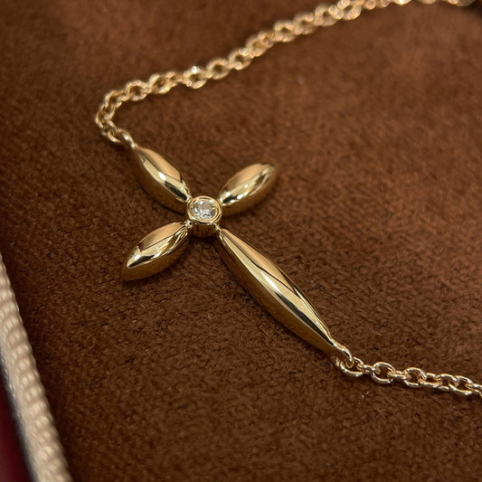 Minimalist 18k gold plated sterling silver cross bracelet laid on brown fabric for wholesale product catalog
