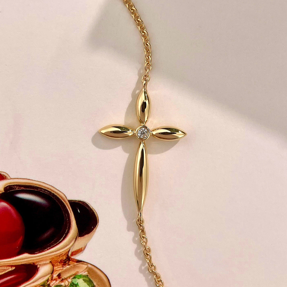 Vertical view of dainty gold cross chain bracelet with sparkling cz stone on white background