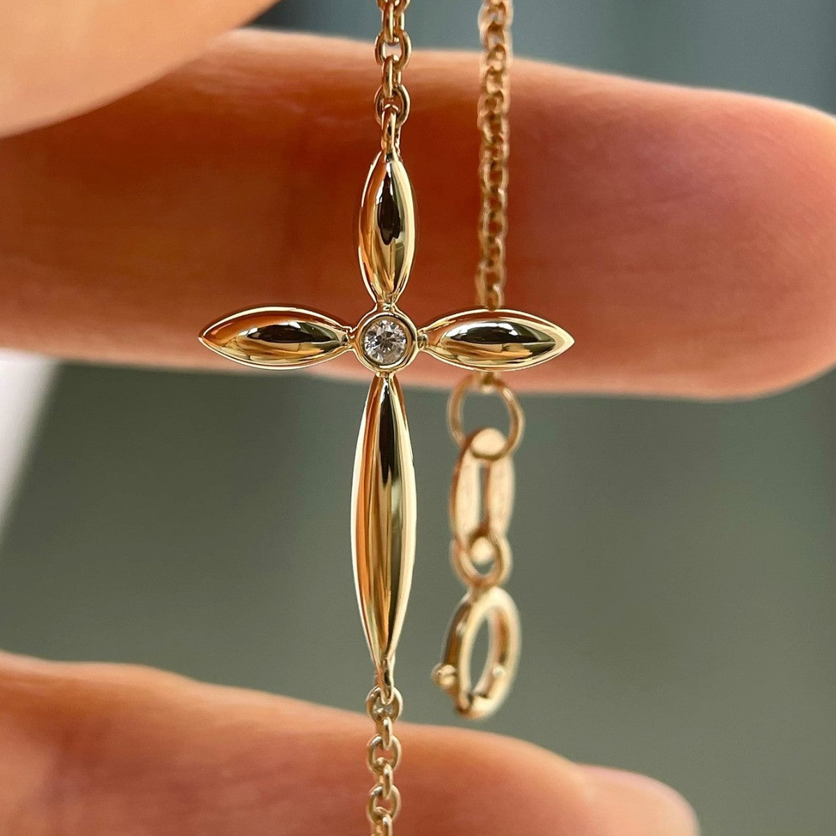 Close up of S925 gold plated silver marquise cross charm with single center cz held by fingers