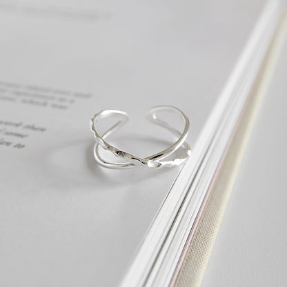 Adjustable sterling silver crossover ring displayed on book page, open ring style available for wholesale minimalist jewelry collections