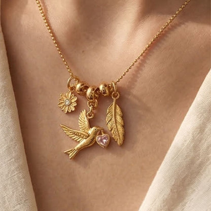 Model wearing gold tone bird leaf flower charm necklace with pink heart crystal accent