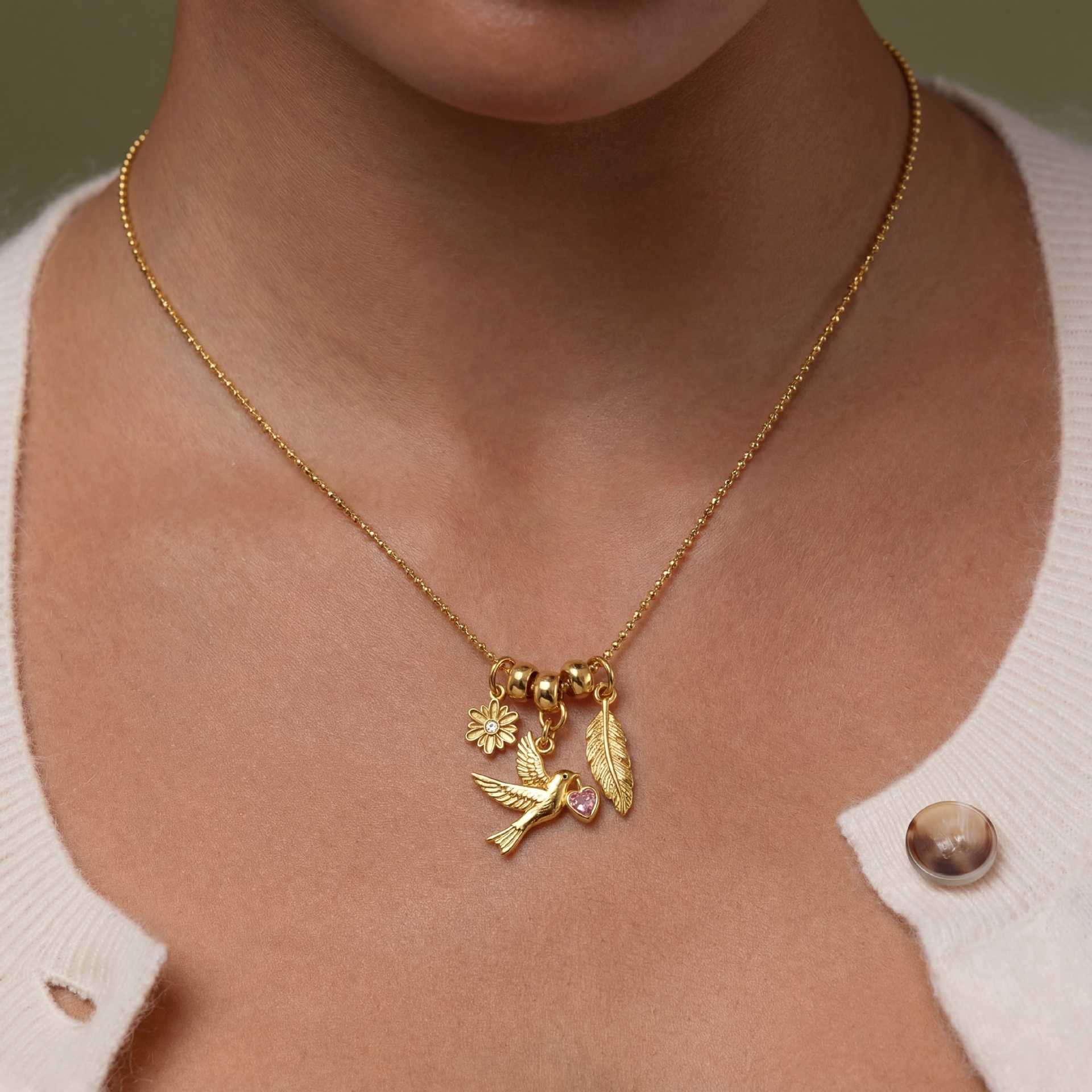 Gold tone charm necklace with bird leaf flower charm and pink heart crystal accent