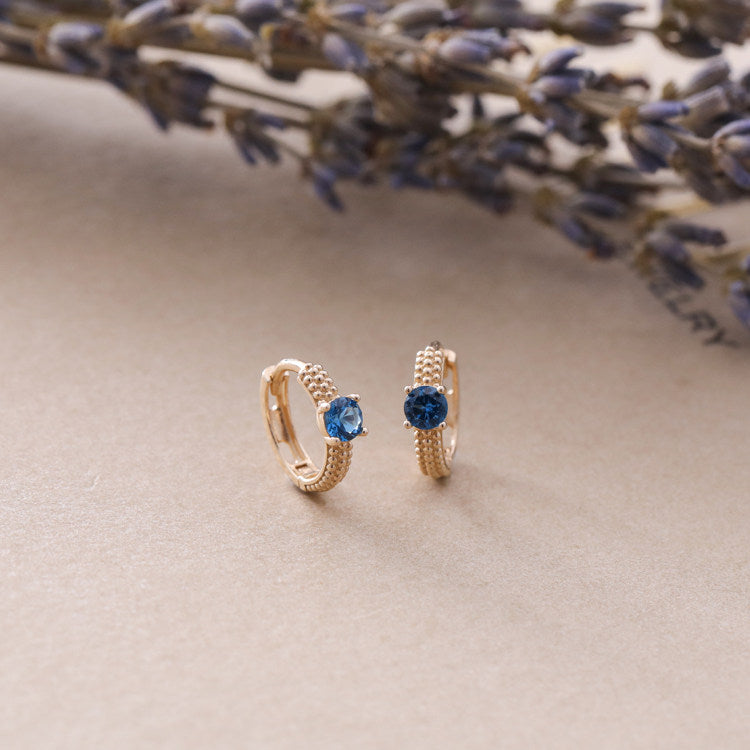 Close up of S925 sterling silver vintage style huggie earrings featuring sapphire blue cubic zirconia stones