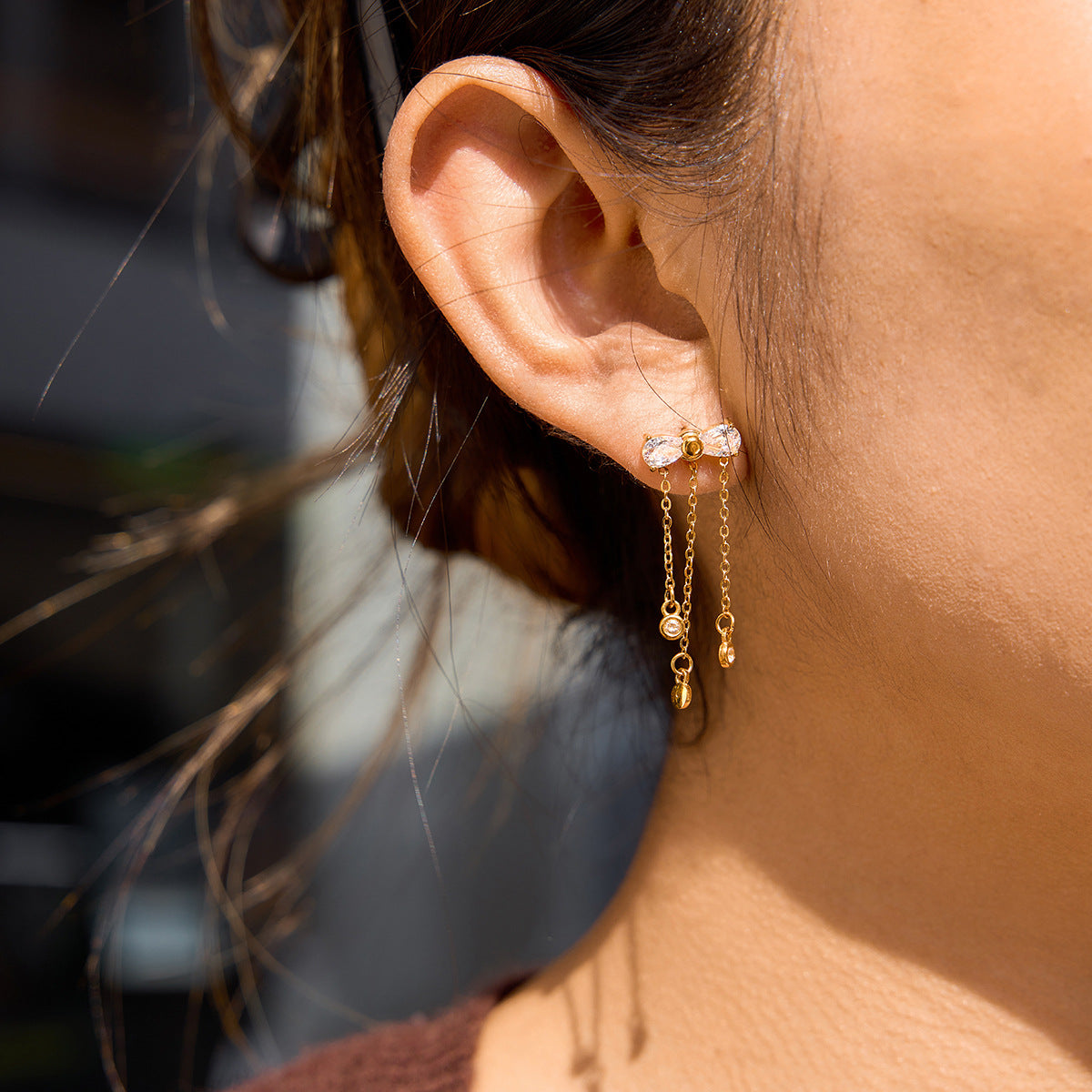 Model wearing gold bow tassel earrings with dangling chain and zircon sparkle