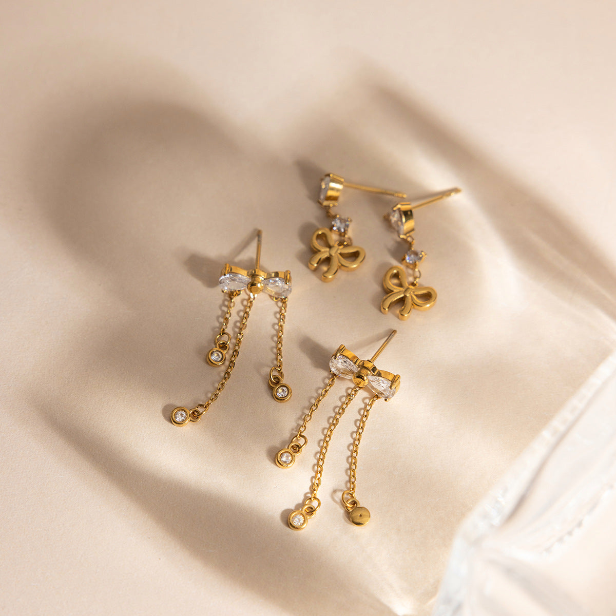 Gold tone bow tassel drop earrings with teardrop zircon stones on soft fabric background