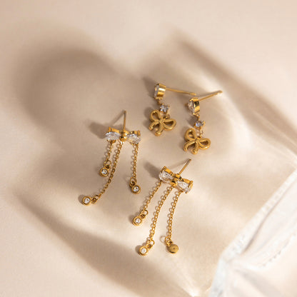 Gold tone bow tassel drop earrings with teardrop zircon stones on soft fabric background