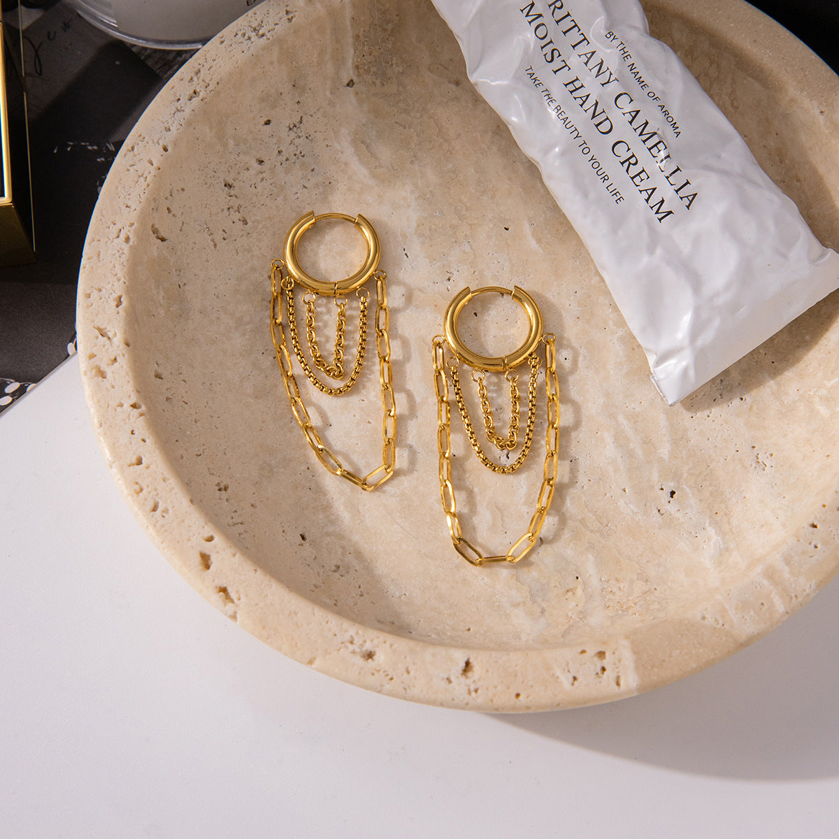 Gold tone hoop earrings with layered chain tassels displayed on stone tray