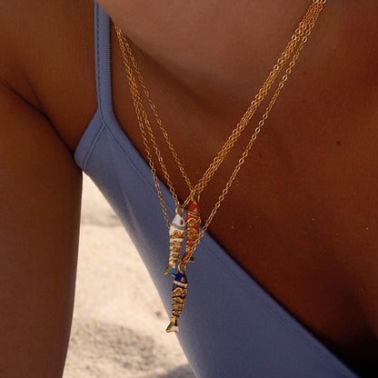 Layered gold tone fish pendant necklaces worn for a coastal summer look
