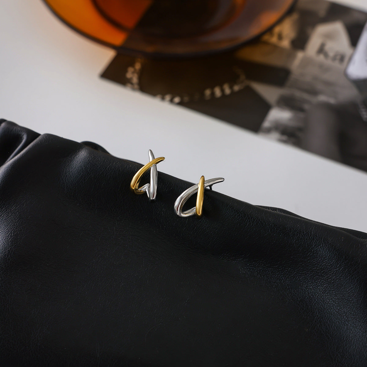Gold and silver crossed line stainless steel earrings on black pouch background