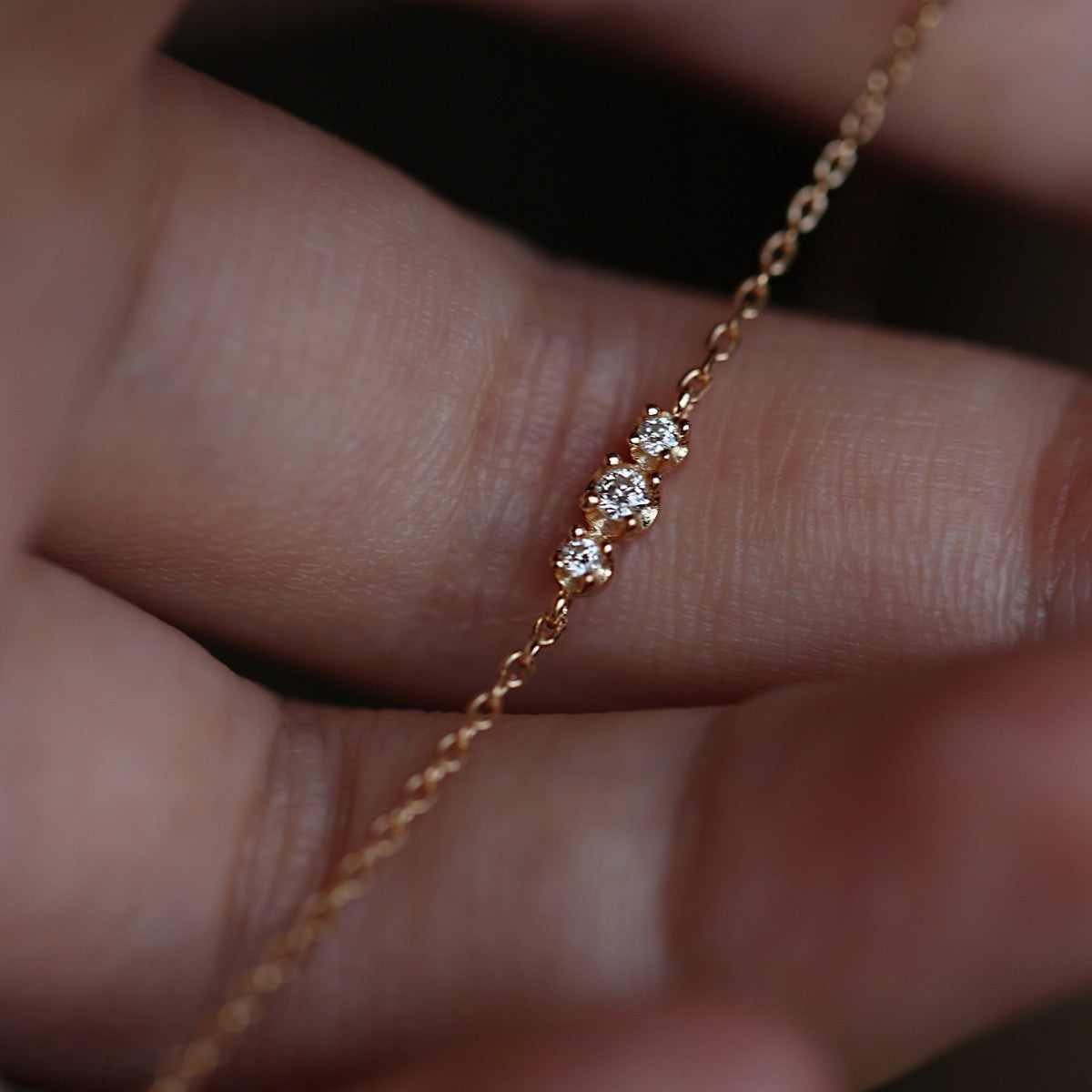 Close up of three sparkling cubic zirconia stones on an ultra thin gold chain bracelet for retail catalog