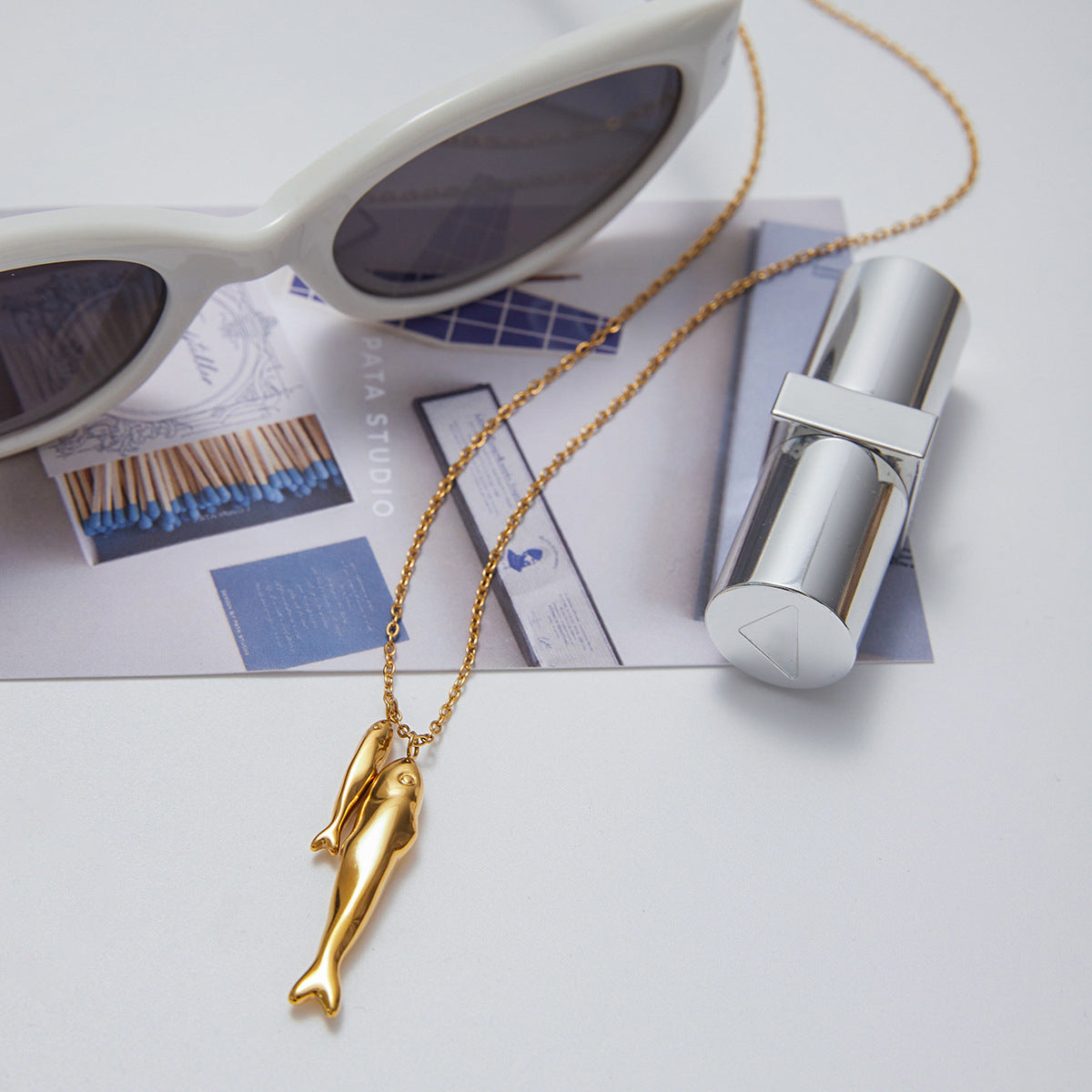 Double fish pendant necklace styled with sunglasses and lifestyle props