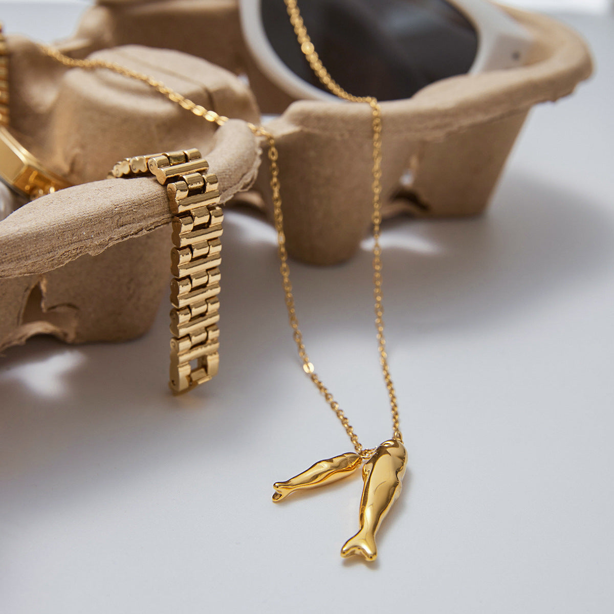 Gold tone stainless steel double fish necklace flat lay with accessories