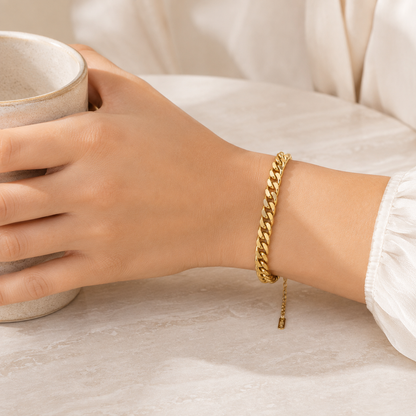Gold curb chain bracelet worn on the wrist in a neutral lifestyle setting
