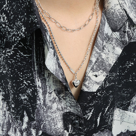 Model wearing layered silver heart pendant necklace with mixed chain design, ideal for minimalist jewelry wholesale styles.