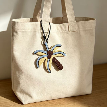 Blue and yellow palm tree charm attached to a cream canvas tote bag