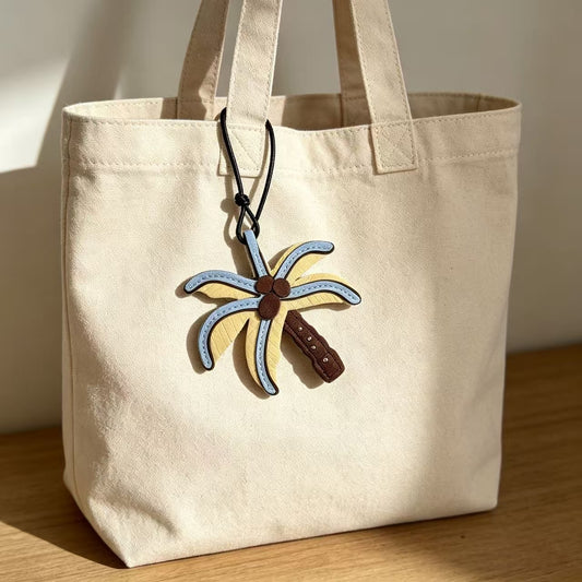 Blue and yellow palm tree charm attached to a cream canvas tote bag