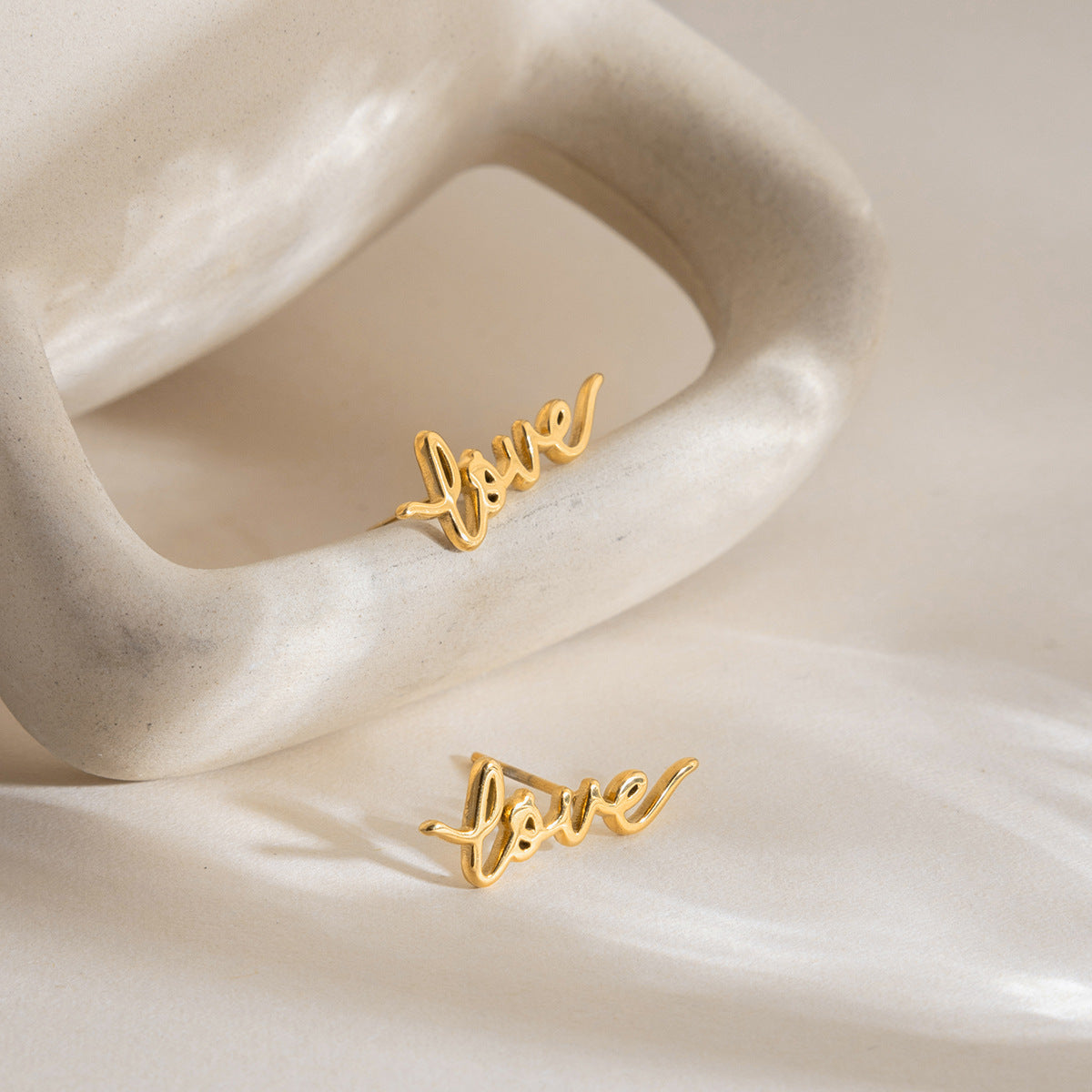 Gold stainless steel love letter stud earrings styled on shell display
