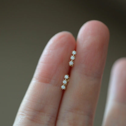 
Close up of miniature huggie earrings featuring three sparkling cubic zirconia stones in a vertical arrangement