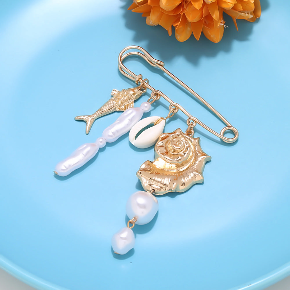 Gold tone safety pin brooch featuring conch shell cowrie shell fish and pearl charms
