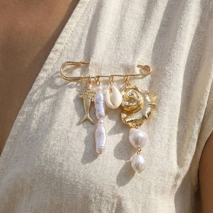 Gold tone ocean safety pin brooch with fish shell and pearl charms worn on a linen dress