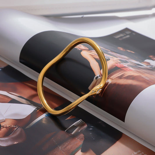 Snake inspired gold open cuff bracelet displayed on magazine background