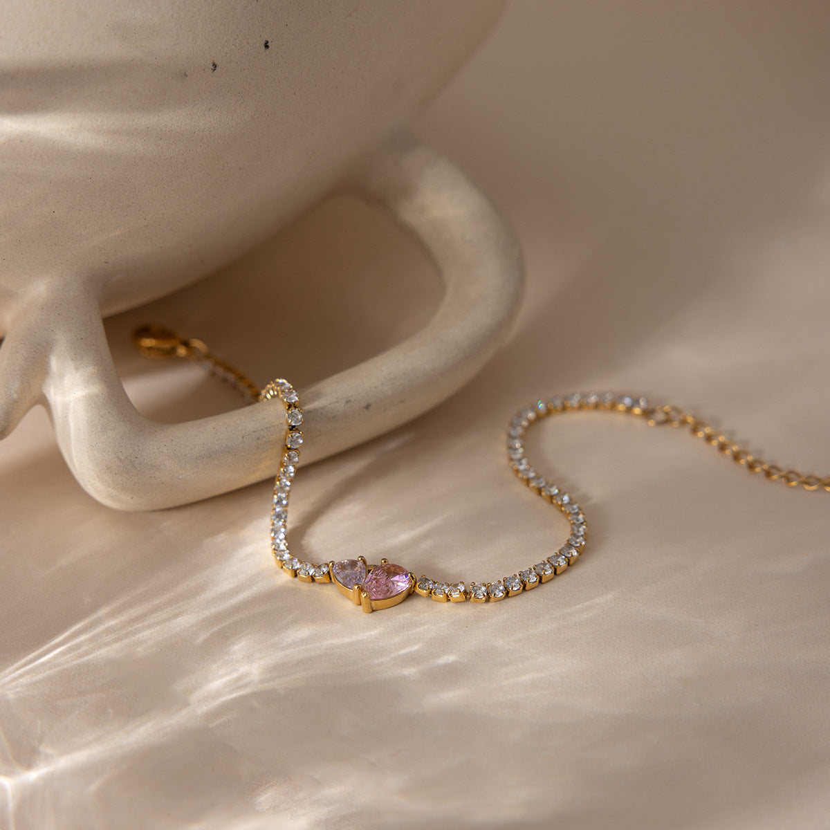 Gold tennis bracelet with pink heart zircon on display surface