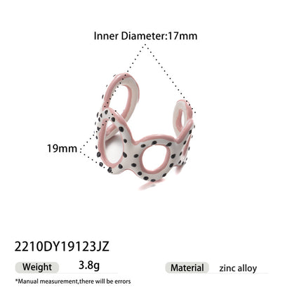 Pink and white enamel ring with black polka dots and hollow design.