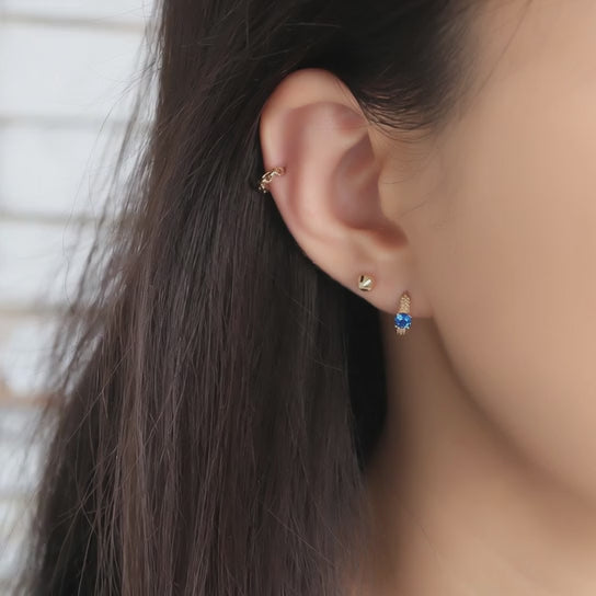 Rotating view of S925 sterling silver blue sapphire huggie earrings with 18K gold plating for wholesale jewelry buyers and boutique collections