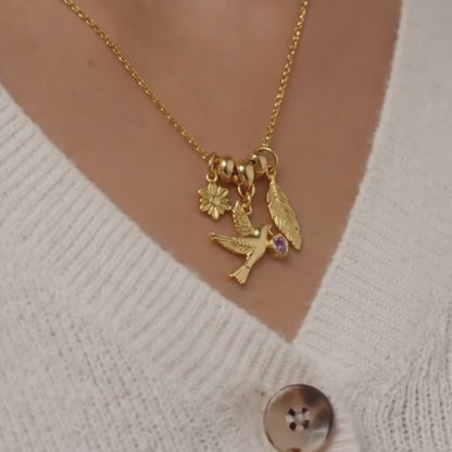 Gold tone charm necklace displayed on textured stone with angel charm heart crystal and heart lock pendant