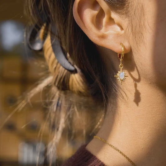 close up video of gold stainless steel hoop earrings with white opal star pendant and crystal details