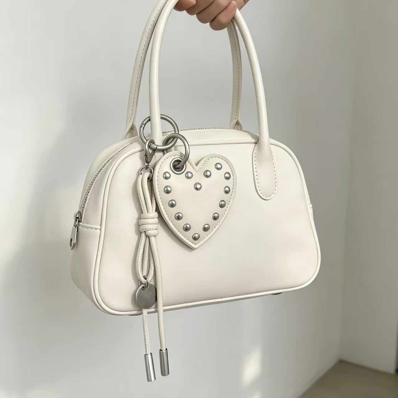 Ivory PU leather heart charm with tassel attached to a white handbag
