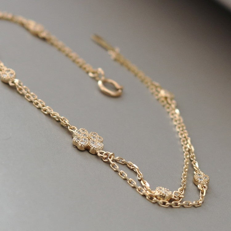 Flat lay of an S925 double chain bracelet with a four petal cubic zirconia centerpiece and round stone stations