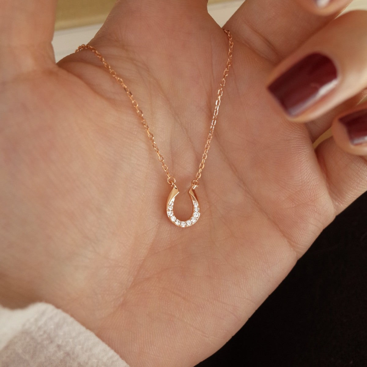 S925 gold plated horseshoe pendant necklace held in hand with sparkling zircon details