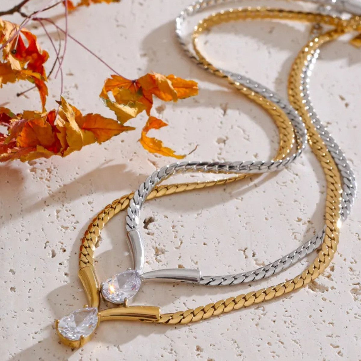 gold and silver teardrop zircon snake chain necklaces displayed on table
