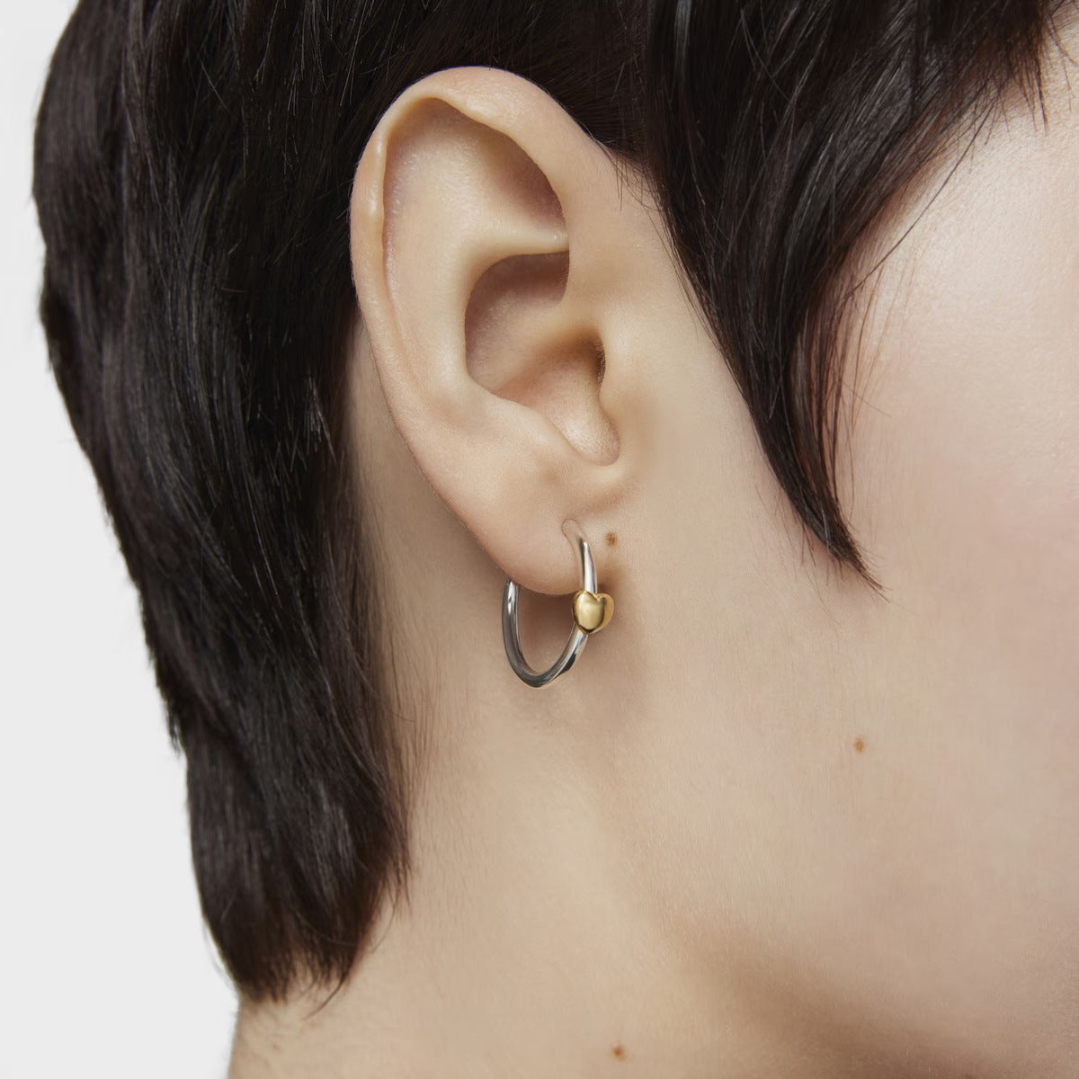 Model wearing two tone stainless steel heart hoop earrings