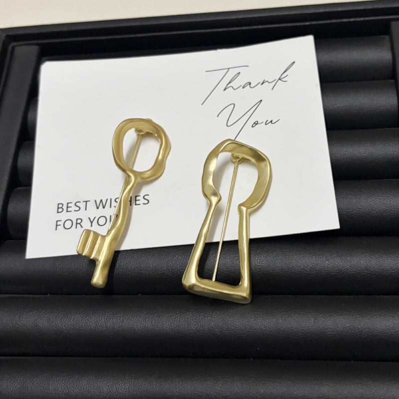 Gold abstract key and keyhole brooches displayed on a gift card