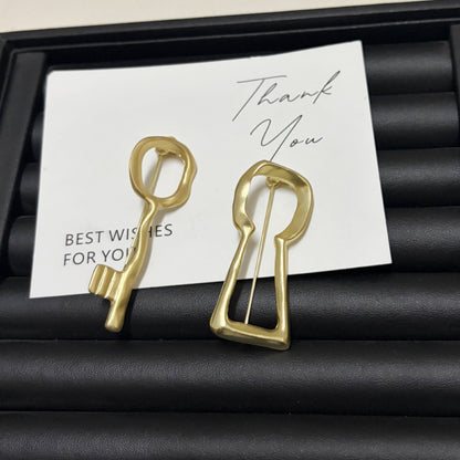 Gold abstract key and keyhole brooches displayed on a gift card