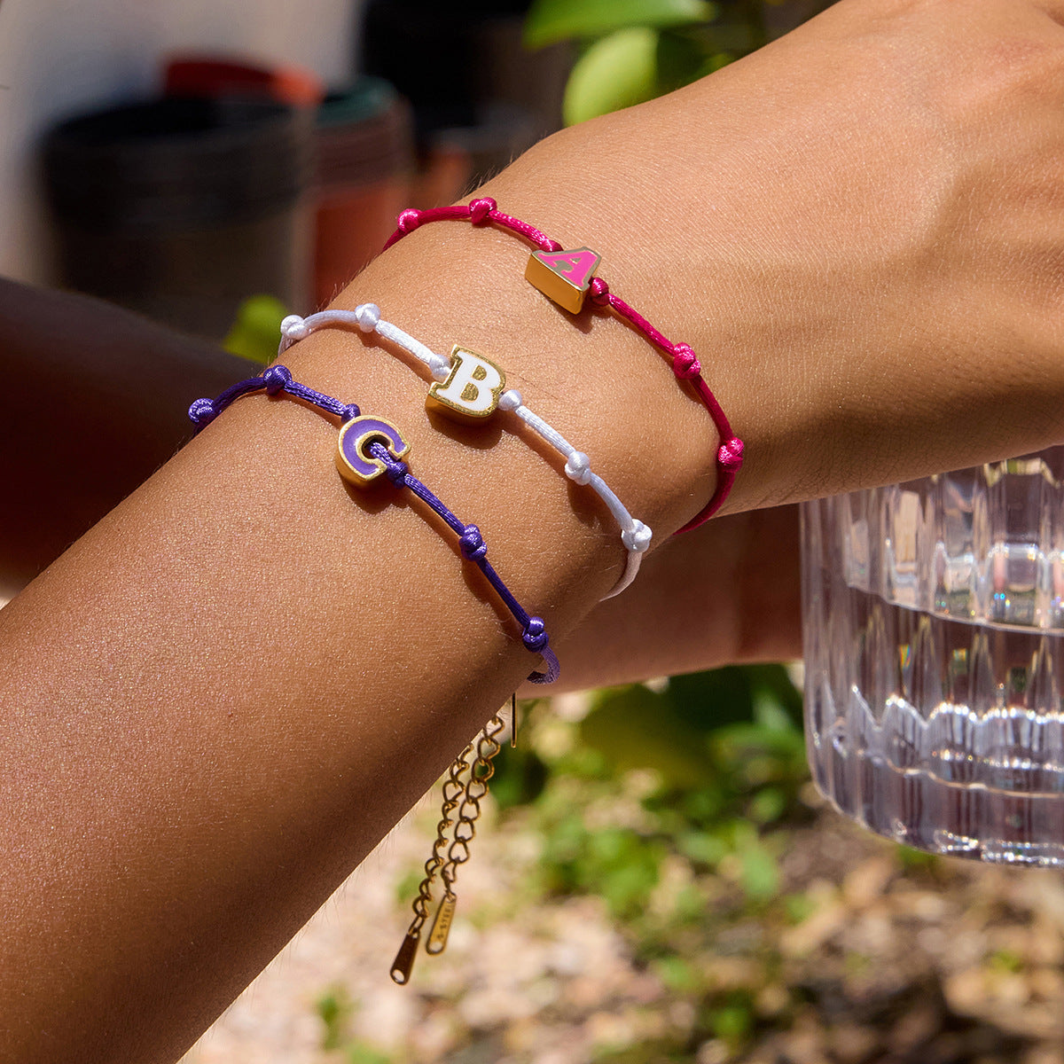 Model wearing three personalized letter bracelets with A, B, and C enamel charms. These wholesale 18k gold plated friendship bracelets are ideal as custom jewelry gifts for her or boutique resale.