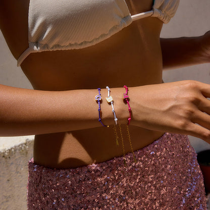 Outdoor lifestyle shot of a woman stacking adjustable friendship bracelets in bulk featuring enamel A, B, and C initials. Stylish letter bracelets for women, ideal for fashion bracelet wholesale.