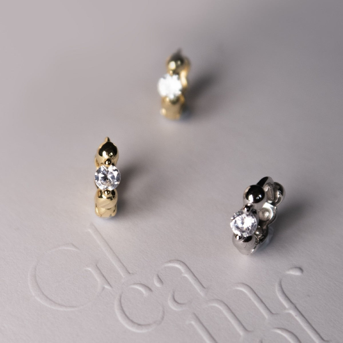 Close up of sterling silver huggie earrings featuring sparkling cubic zirconia and polished bead details