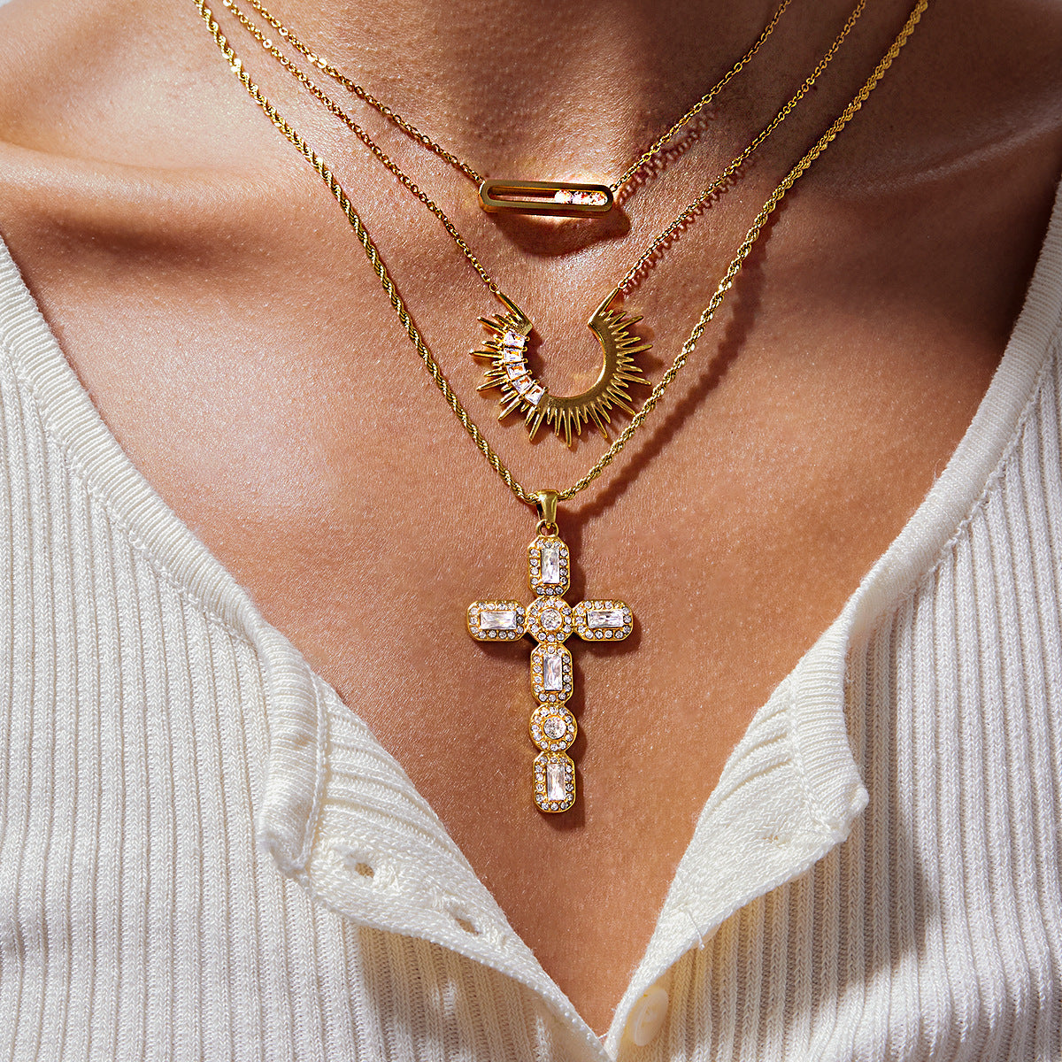 Gold cubic zirconia cross necklace layered with celestial and bar pendant necklaces
