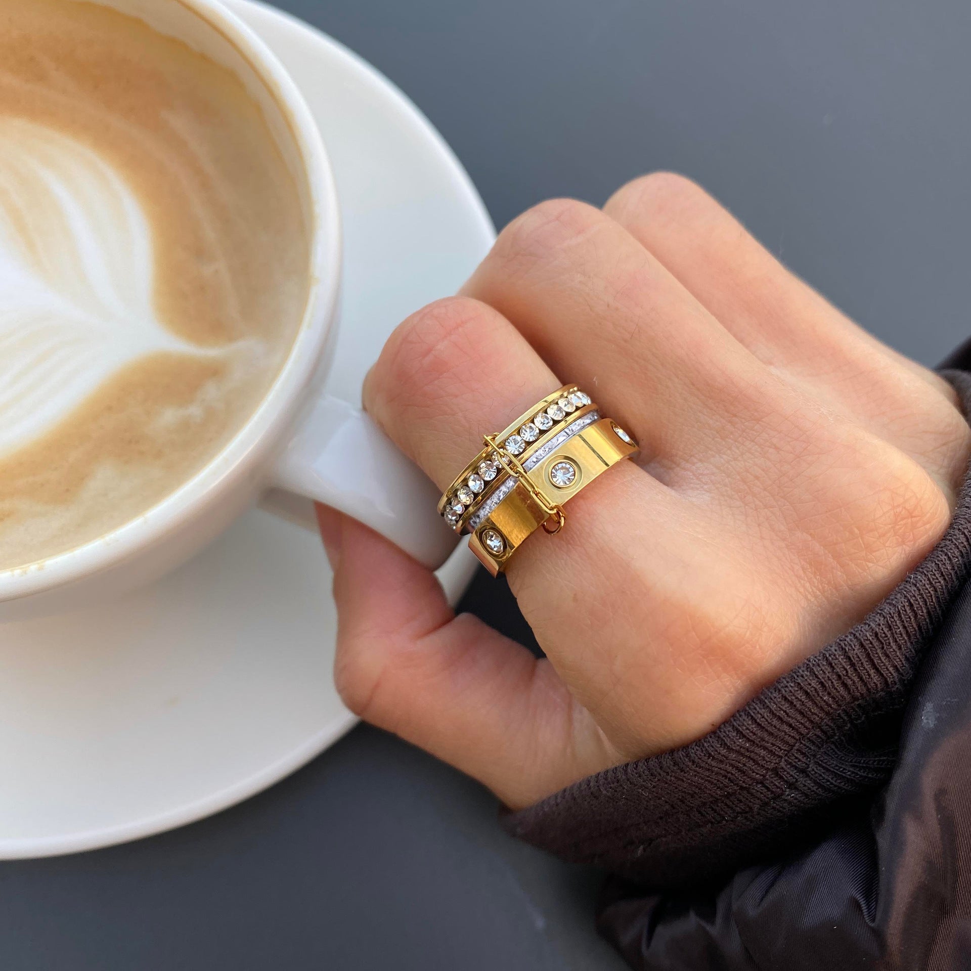 Woman wearing gold and silver zircon stainless steel five piece ring set beside coffee cup